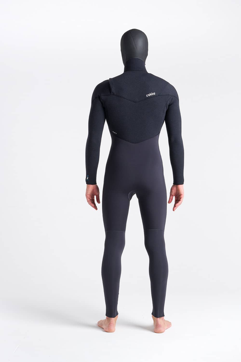 A person stands barefoot facing away, wearing the C-Skins Men’s ReWired 5/4mm Hooded Wetsuit against a plain white background. The wetsuit covers their entire body except for the feet and hands.