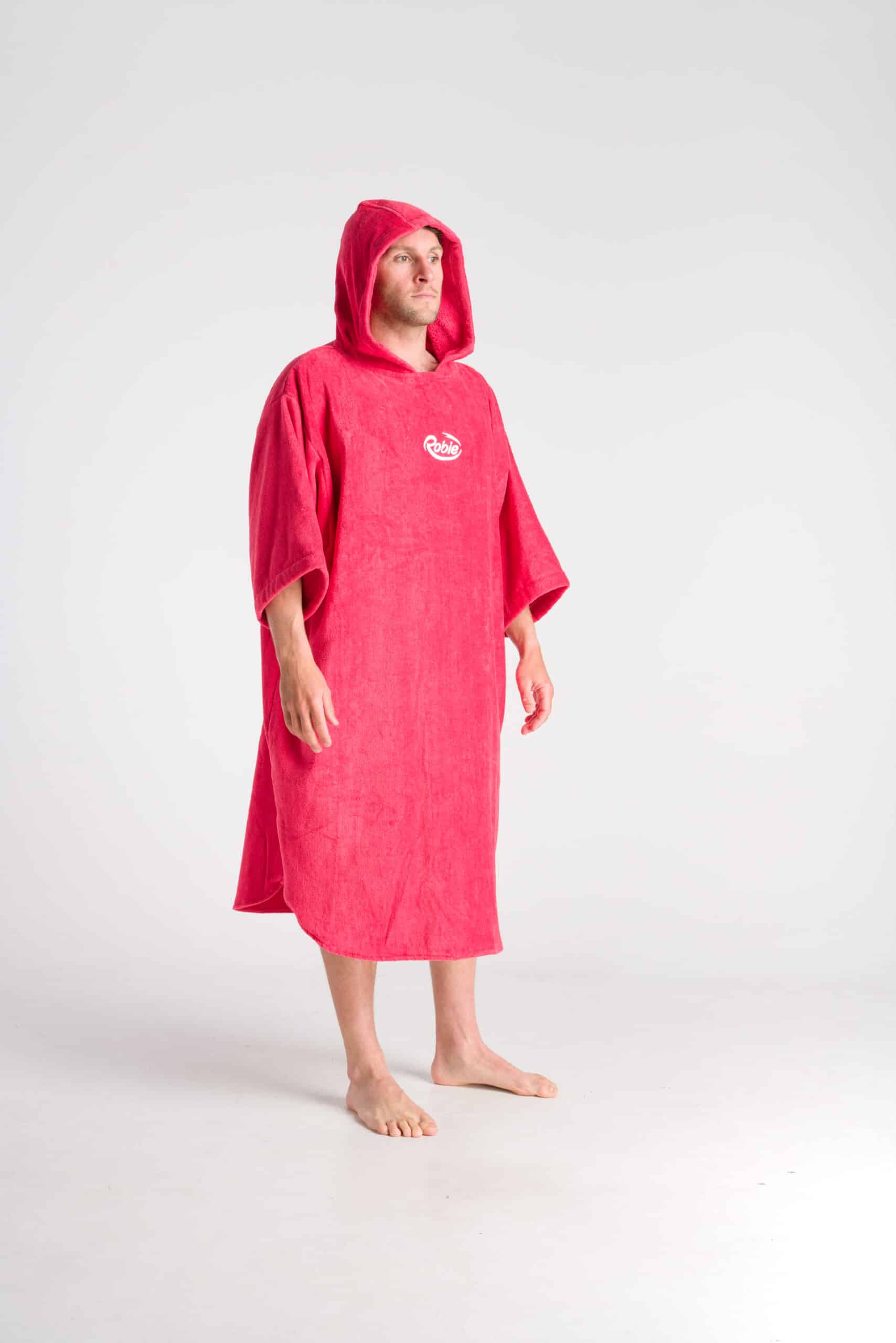 A person stands barefoot in a bright pink Robie Long Sleeve Towel Robe, knee-length with a hood, short sleeves, and a small white chest logo, set against a plain white background.