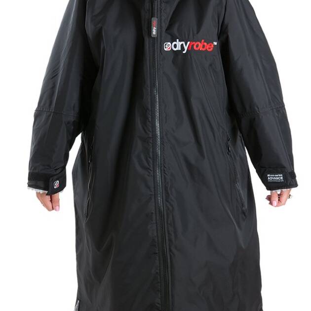 A person stands barefoot wearing a Dryrobe Advance Long Sleeve Black/Grey coat with a chest logo, zipped up and featuring long sleeves, against a plain white background.