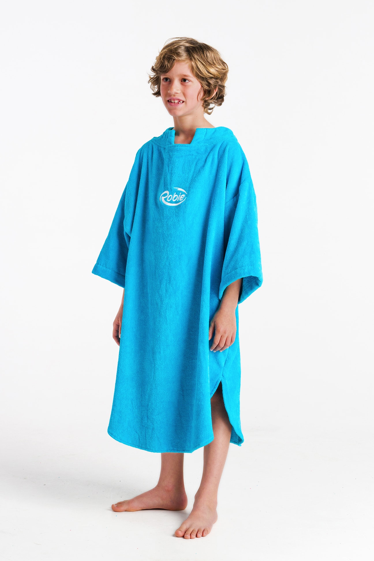 A smiling young child with short, wavy blond hair stands barefoot on a white background, wearing a bright blue Robie Long Sleeve Towel Robe with "Robie" on the chest.