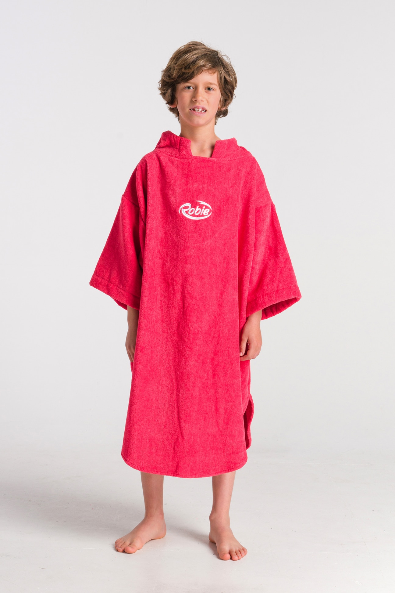 A young boy with light brown hair stands barefoot on a white background, wearing a Robie Long Sleeve Towel Robe in bright pink with "Robie" printed on the front.