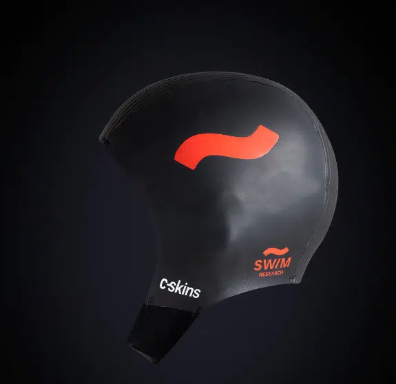 The C-Skins Swim Research 3mm GBS Cap is a black swim cap featuring a red curved stripe and "c-skins" and "SWM RESEARCH" printed in white and orange, with an ergonomic, asymmetrical shape shown on a dark gradient background.