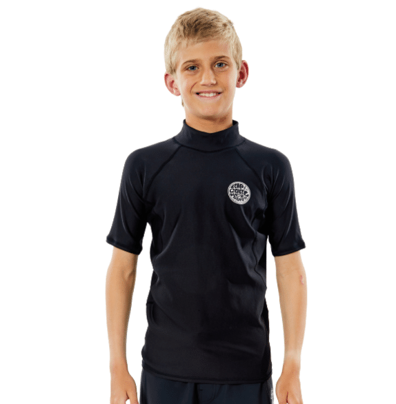 A smiling blonde boy stands against a white background wearing the Ripcurl Isothermie Short Sleeved Rashvest, a black rash vest featuring a small circular logo on the left chest.