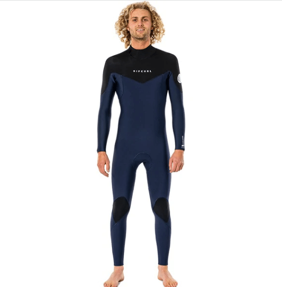 A barefoot person with curly blond hair is wearing the Rip Curl Men's Dawn Patrol 5/3mm Back Zip Wetsuit in navy blue and black, featuring "RIP CURL" on the chest.