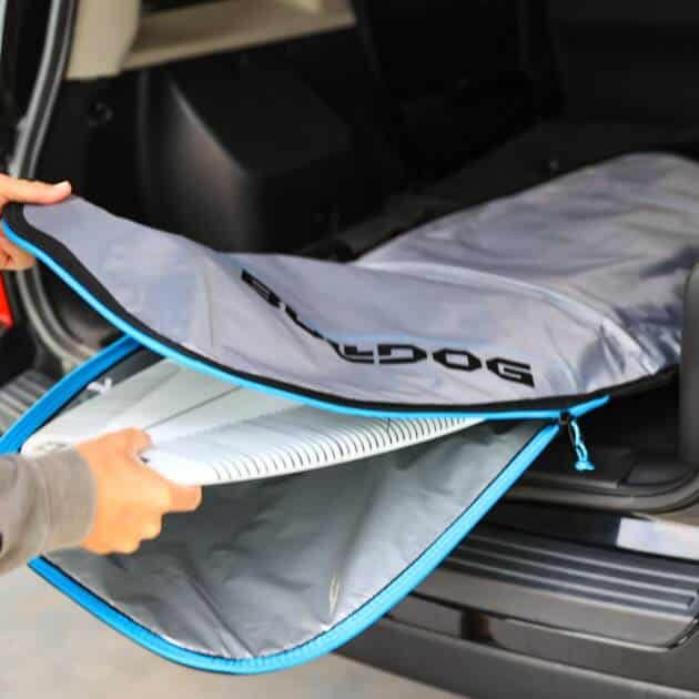 A person loads a Bulldog Board Bag Essential 5mm Fish, padded and zippered, with a surfboard inside into the back of a black SUV with its rear hatch open.