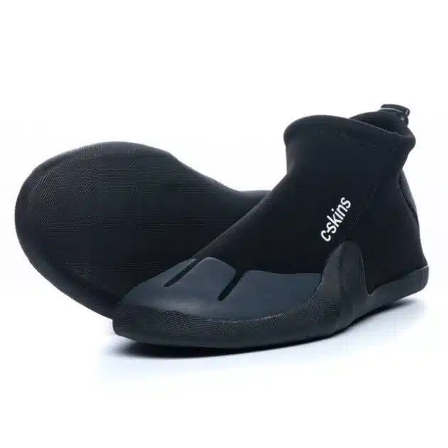A pair of C-Skins Legend 3mm Round Toe Reef Boots in black features a minimalist design with the "C-Skins" logo on the side. One boot stands upright, whilst the other lies sideways displaying its distinctive sole.